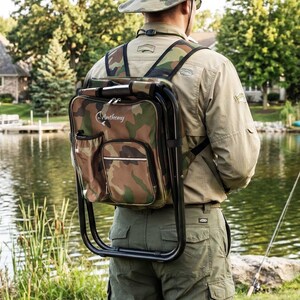 May include: A camouflage print backpack with an integrated black metal folding stool frame. The bag features a front zippered pocket, a side mesh pocket, and the name Anthony printed in white script with a fish graphic on the upper front panel.