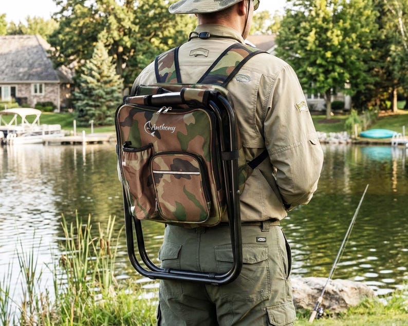 May include: A camouflage print backpack with an integrated black metal folding stool frame. The bag features a front zippered pocket, a side mesh pocket, and the name Anthony printed in white script with a fish graphic on the upper front panel.