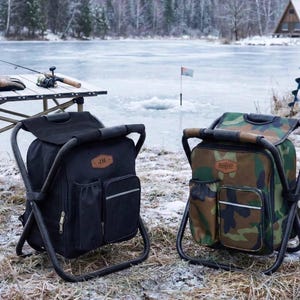 May include: Two portable folding chair backpacks, one in solid black and one in a green, brown, and black camouflage pattern. Each features a metal frame, a main storage compartment, side pockets, and a brown leather-style patch on the front.