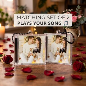 Könnte beinhalten: Ein passendes Set aus zwei quadratischen, transparenten Kunststoff-Schlüsselanhängern, die jeweils ein Foto eines Paares mit einem kleinen Hund zeigen. Der Text MATCHING SET OF 2 PLAYS YOUR SONG steht über den Anhängern mit schwarzen Perlenketten.