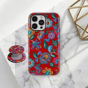 Puede incluir: Una funda de teléfono roja y un soporte a juego con un colorido estampado floral en azul, amarillo y verde. La funda está diseñada para un teléfono inteligente y el soporte está adherido a la parte posterior.