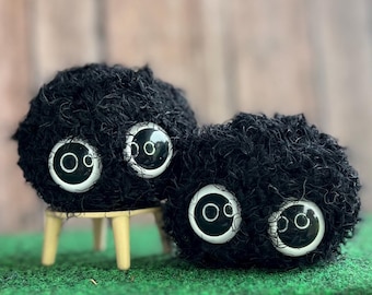 Könnte beinhalten: Zwei schwarze, flauschige Plüschtiere mit großen weißen Augen. Die Spielzeuge sitzen auf einem kleinen Holzhocker. Der Hintergrund ist ein verschwommenes Bild einer Holzoberfläche.
