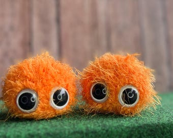 Könnte beinhalten: Zwei orangefarbene, flauschige Kreaturen mit großen schwarzen Augen. Die Kreaturen bestehen aus weichem, flauschigem Material und haben einen verspielten Ausdruck.