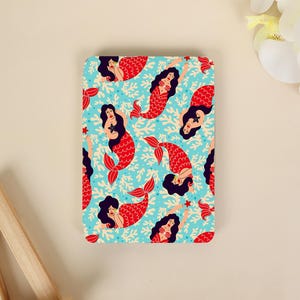 May include: A rectangular card featuring a repeating pattern of mermaids with dark hair and red tails swimming among light-coloured coral branches on a bright blue background. The mermaids are depicted in various poses, some holding small starfish.