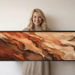 Könnte beinhalten: Ein rechteckiges Wandbild mit einem abstrakten Landschaftsmotiv, das geschichtete Texturen in Terrakotta, gebranntem Orange, Dunkelbraun und Cremetönen aufweist. Das Kunstwerk ist in einem dünnen schwarzen Rahmen im Querformat eingefasst.