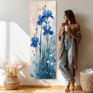 Op de afbeelding: Een verticale canvas print met blauwe irissen in aquarel stijl tegen een beige achtergrond. Het kunstwerk toont gedetailleerde bloemblaadjes en stelen met blauwe en witte accenten, wat een serene bloemenscène creëert.