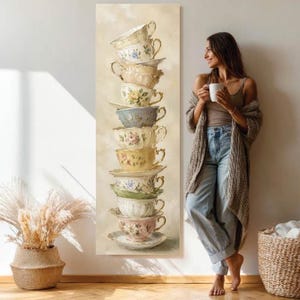 Könnte beinhalten: Ein vertikaler Wandkunstdruck, der einen hohen, wackeligen Stapel aus zehn Vintage-Teetassen und Untertassen aus Porzellan zeigt, die jeweils mit zarten Blumenmustern in sanften Pastellfarben vor einem neutralen, cremefarbenen Hintergrund verziert sind.