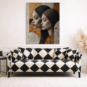 Op de afbeelding: Een abstracte kunstprint met twee vrouwenprofielen tegen een achtergrond van neutrale tinten en geometrische vormen. Het kunstwerk hangt boven een zwart-witte ruitjesbank met bijpassende kussens.