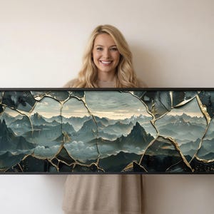 Könnte beinhalten: Gerahmter Landschaftskunst-Druck mit einer Berglandschaft in Teal- und Grautönen. Das Kunstwerk hat einen Riss-Effekt mit goldenen Akzenten, eingefasst in einen schwarzen Rahmen. Das Thema ist Natur und Landschaft.