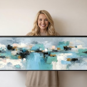 Op de afbeelding: Abstracte kunstafdruk in een zwarte lijst. Het kunstwerk toont een landschap van turquoise, blauwe, zwarte, gouden en witte penseelstreken. Het schilderij heeft een lange, rechthoekige vorm, perfect voor een woonkamer of slaapkamer.