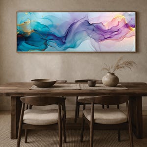 May include: Abstract art print in a rectangular wooden frame. The artwork features flowing, colorful swirls of teal, blue, purple, and gold. The painting hangs above a wooden dining table with chairs, a centerpiece, and other decorative items.