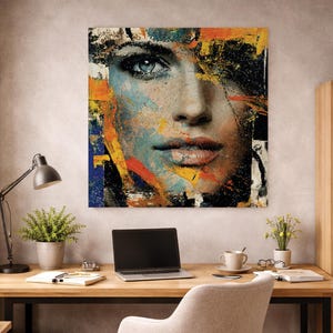 Può includere: Stampa artistica astratta raffigurante il volto di una donna con occhi blu e labbra rosse. L'opera d'arte utilizza un mix di colori tra cui blu, arancione, giallo e nero, con pennellate e spruzzi visibili. L'opera è esposta su una parete sopra una scrivania in legno.
