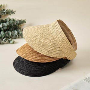 May include: A stack of three straw visors in light beige, medium tan, and black. Each visor features a wide, curved brim with a woven texture and an open-top design, allowing for a comfortable fit while providing shade for the face.
