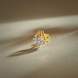 May include: A gold stud earring shaped like a trident, featuring a polished yellow gold finish and a central section encrusted with small, clear, sparkling stones. The design includes three prongs pointing upward, with a secure screw-back post mechanism.