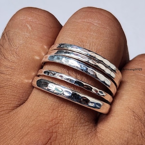 May include: A set of four stacked silver rings, each featuring a distinct hammered texture with a polished, reflective finish. The bands are uniform in width and sit closely together, showcasing a metallic sheen across the curved surfaces.