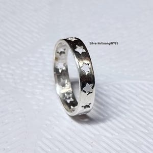 May include: A silver ring with a repeating star pattern. The ring is made of a shiny, metallic material and features cut-out star shapes around the band. The ring is a simple, yet elegant piece of jewelry.
