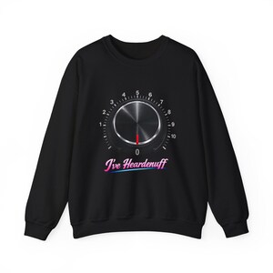 Może przedstawiać: Czarna bluza z nadrukiem srebrnej tarczy z czerwoną wskazówką, ponumerowaną od 0 do 10. Pod tarczą napis "I've Heardenuff" w stylu retro. Bluza ma długie rękawy.