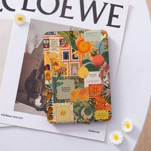 May include: A patterned journal with a collage design. The design includes a sun, flowers, and text. The journal features yellow, orange, and green hues. Text includes phrases like "Please love yourself" and "Actually, life is beautiful and I have some."