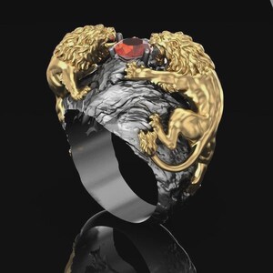 Könnte beinhalten: Ein Ring mit zwei goldfarbenen Löwen, die sich gegenüberstehen und auf einer strukturierten, dunkelgrauen, felsartigen Ringschiene angebracht sind. Ein einzelner, facettierter, runder, roter Edelstein sitzt zwischen den Köpfen der Löwen.