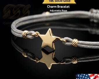 May include: A 14K solid gold charm bracelet with an adjustable rope design. The bracelet features a gold star charm and gold accents. The gray rope is woven, and the bracelet is displayed on a reflective black surface.