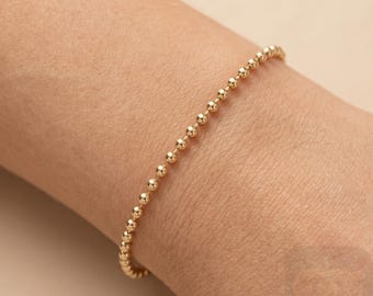May include: A delicate gold beaded bracelet. The bracelet is composed of small, evenly spaced, round beads. The jewelry is displayed on a person's wrist, showcasing the bracelet's design and color. The bracelet is a simple yet elegant accessory.