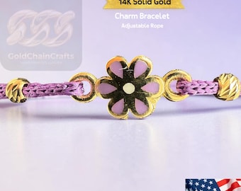 May include: A close-up of a 14K solid gold charm bracelet with an adjustable rope. The bracelet features a gold flower charm with purple petals. The rope is a light purple color. The text "14K Solid Gold Charm Bracelet Adjustable Rope" is visible.
