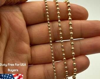 May include: Close-up of three strands of 14K solid gold ball chain necklaces. The chains are held in a hand, showcasing the delicate, shiny, and uniform spheres. The text "14K Solid Gold" is displayed at the top.