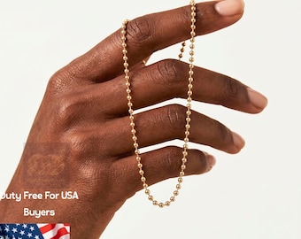May include: A delicate 14K solid gold ball chain necklace. The necklace is held by a hand against a white background. The text "14K Solid Gold" is displayed above the necklace.