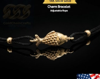 May include: A 14K solid gold charm bracelet with an adjustable black rope. The bracelet features a detailed gold fish charm and gold beads. The text on the image reads "Charm Bracelet Adjustable Rope".