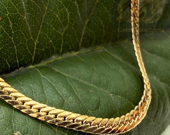 May include: A gold-colored chain necklace with a flat, interlocking design. The necklace is displayed on a large, green leaf. The text "Gold Rain Crafts" is visible in the background.