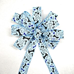 May include: A blue ribbon bow with a black and white paw print and bone pattern. The bow is tied in a knot and the tails are hanging down.