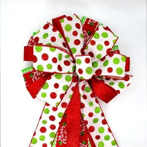 May include: A festive Christmas bow with red, white, and green polka dots. The bow features a layered design with glitter accents and the words "Merry Christmas" printed on the red ribbon. Perfect for holiday decorations.