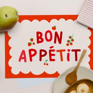 Peut inclure: Nature morte avec une poire verte, une carte avec l'inscription "BON APPÉTIT" en rouge et une cuillère en bois. La carte a une bordure blanche festonnée et est ornée d'illustrations de fraises et de cerises.