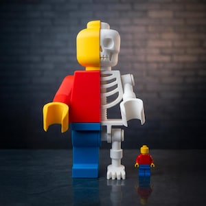 May include: A large, segmented toy figure, half yellow and red, and half white skeleton, stands next to a smaller version of itself. The larger figure has blue legs and yellow hands. The background is a dark, textured surface.
