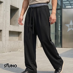 May include: Black sweatpants with a drawstring waist and a plaid waistband. The pants have a relaxed fit and pockets. The image also shows the text "Aldrix STUDIO".