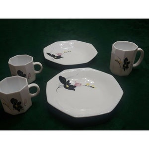 May include: A set of white ceramic dinnerware with a floral design. The set includes two octagonal mugs and two octagonal plates with a black and pink floral design.