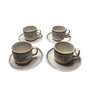 May include: Set of four white ceramic teacups and saucers with a floral design. The cups and saucers have a green and pink floral pattern.