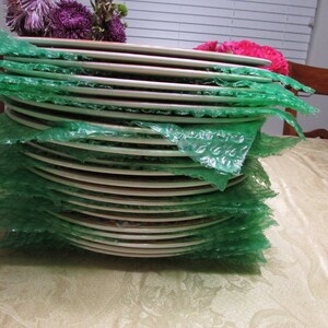 May include: A stack of white ceramic plates wrapped in green bubble wrap. The plates are stacked on top of each other and are ready to be shipped.