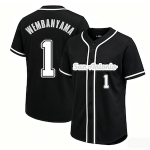 May include: Black baseball jersey with white trim and the number 1. The jersey has "WEMBANYAMA" on the back and "San Antonio" on the front. The jersey is button-down with short sleeves.
