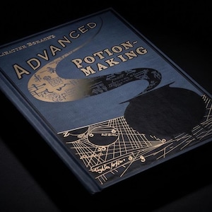 Puede incluir: Un libro de tapa dura titulado "Advanced Potion Making" con letras e ilustraciones doradas sobre una cubierta azul oscuro. El libro está sobre un fondo negro, con el título en un lugar destacado.