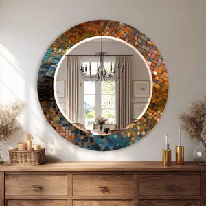 May include: A round decorative mirror with a mosaic tile design in shades of orange, blue, and brown. The mirror is set against a white wall and is above a wooden dresser. The mirror's frame has a textured appearance.