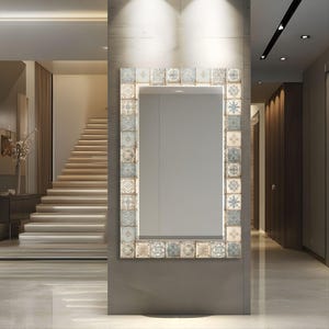 Puede incluir: Un espejo de pared rectangular con un marco decorativo compuesto por azulejos cuadrados individuales. Cada azulejo muestra un patrón intrincado y único en tonos apagados de azul, beige, crema y gris, creando un borde de mosaico.