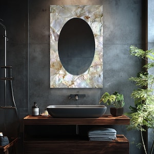 May include: An oval mirror with a mother-of-pearl frame hangs above a dark gray sink. The sink sits on a dark wood vanity with a lower shelf. A small potted plant and towels are on the vanity. The bathroom has dark gray tile walls.