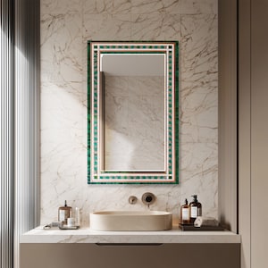 May include: A rectangular mirror with a green and copper-colored mosaic border is mounted on a marble-patterned wall. The mirror is above a beige countertop with a matching oval sink. The bathroom features a modern design with neutral tones.
