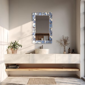May include: A rectangular wall mirror featuring a mosaic frame constructed from various shards of blue and white ceramic pottery. The frame displays a mix of floral patterns and solid white pieces, creating a textured, fragmented border around the glass.