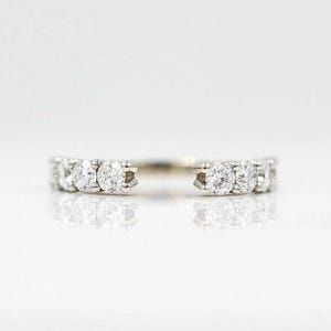 May include: A white gold ring with a series of round, clear diamonds set in a row. The ring has an open design, with the diamond settings on either side of the opening. The ring is set against a white background.