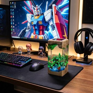 May include: A desktop setup featuring a computer monitor displaying a Gundam image, a keyboard, mouse, and a decorative resin block with a miniature Gundam model inside. The setup includes figurines and a headset.