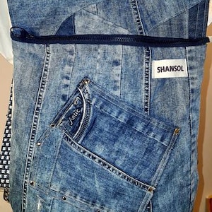 May include: A blue denim backpack with a front pocket and a zipper closure. The backpack is made from recycled denim and features the brand name "SHANSOL" on a white label. The front pocket has the word "Antic" on it.