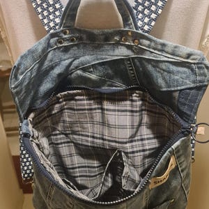 May include: A denim backpack with a plaid interior and a zipper closure. The straps are a blue and white checkered pattern. The bag has a top handle and a small pocket on the front. The interior is gray and black plaid.