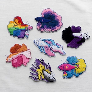 Könnte beinhalten: Gestickte Aufnäher mit farbenfrohen Kampffisch-Designs. Jeder Aufnäher zeigt ein einzigartiges Farbschema, darunter Regenbogen, Lila, Rosa, Blau und Gelb. Die Aufnäher sind mit schimmernden Akzenten versehen, ideal zum Aufpeppen von Kleidung oder Accessoires.
